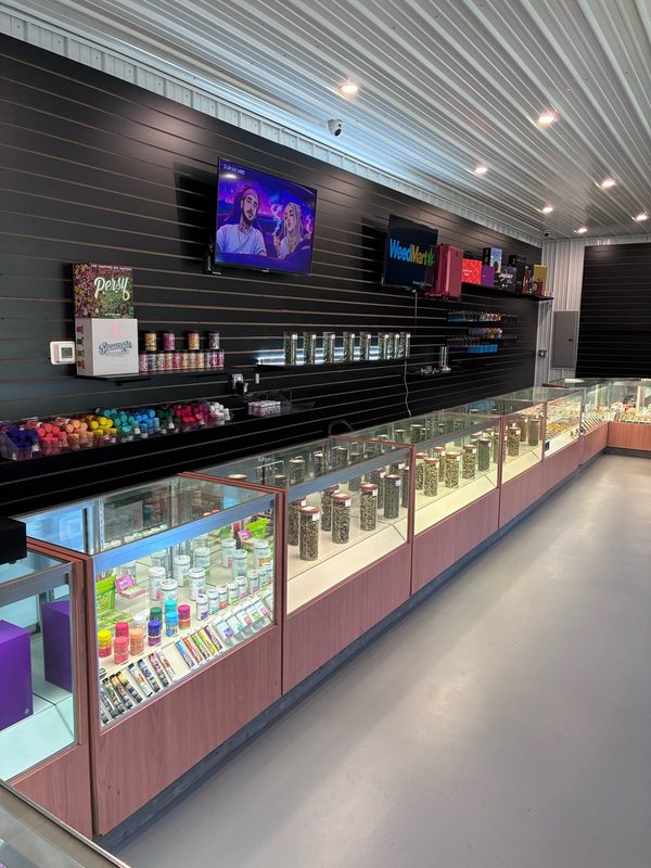 WeedMart counter in Irving, NY with a long row of lit glass display cases and a black slat wall