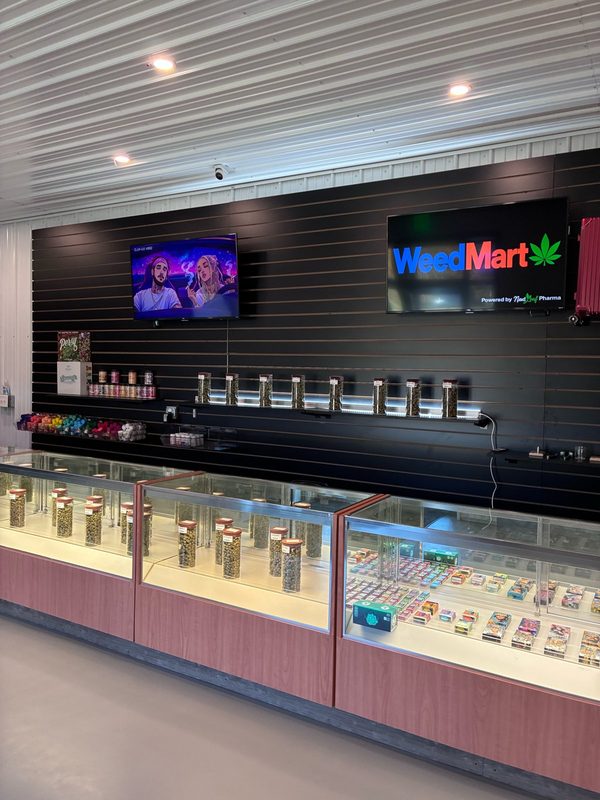 WeedMart sign, powered by Next Leaf Pharma, on a black slat wall above glass display counters inside the Irving, NY shop